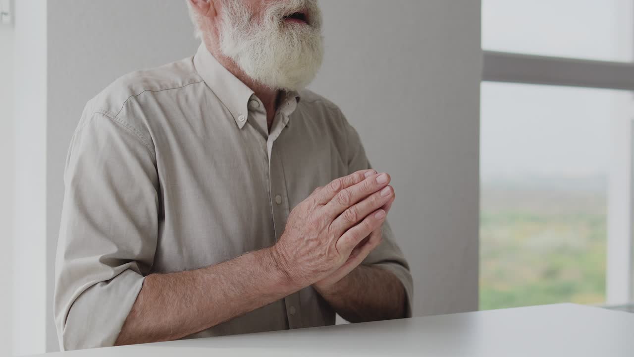 수염을 가진 성숙한 남자가 안경을 쓰고 앉아서 기도하고 축복합니다.