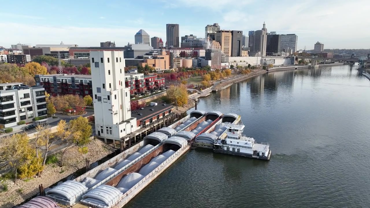 St. Paul, Minnesota'da Mississippi Nehri boyunca bir mavnaya bağlanan bir römorkörün havadan görünümü, arka planda açık bir sonbahar gününde şehir silüeti.