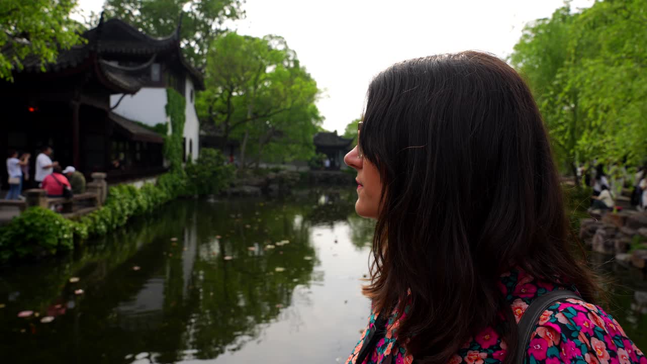 한 여자 는 겸손 한 관리자 의 정원 에서 울창 한 초록색 으로 둘러싸인 조용 한 연못 을 쳐다본다