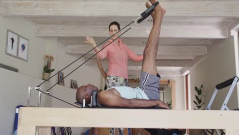 Senior-african-american-man-using-reformer-with-female-pilates-coach,-unaltered,-in-slow-motion