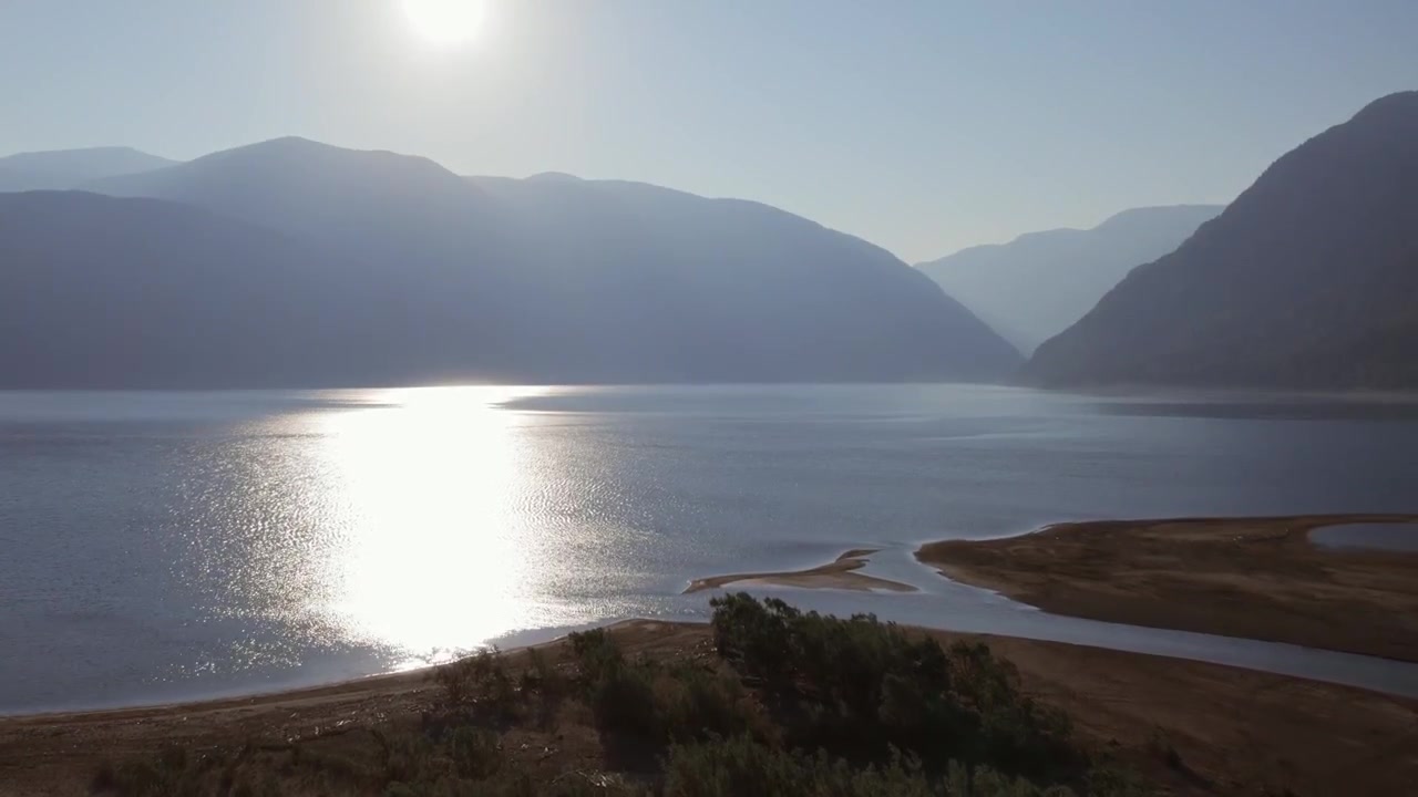 Široký panoramatický pohled na Tělecké jezero s odrazem slunce na klidné vodě, písčitým pobřežím a vrstvenými horami v Altajské republice v Rusku, poklidné přírodní záběry.