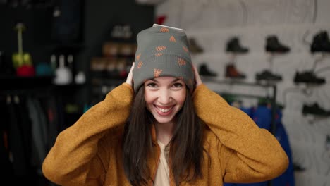 vista frontal de una mujer sonriente probándose un nuevo y colorido sombrero de invierno en una tienda.