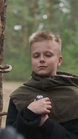 niño adolescente con espada mira al caballero en el campamento militar en cámara lenta del bosque. joven soldado en entrenamiento. preparando nuevos guerreros en la mediana edad