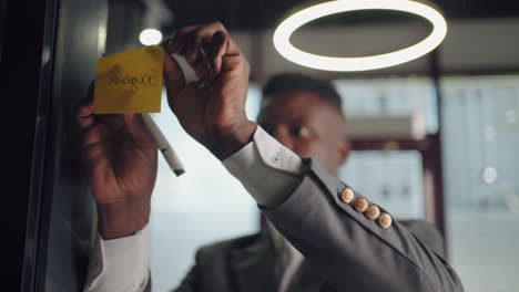 african american businessman working with sticky notes in office. entrepreneur explaining business plan. businessman building mind map with sticky notes on glass