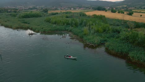 Fisherman-On-Wooden-Boat-In-Lakeshore-With-Lush-Grass-Reeds-In-Lago-Trasimeno,-Italy