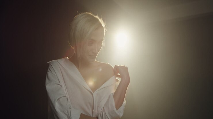 Close-up view of caucasian young female model posing in the dark studio with smoke while the photographer taking shots of her