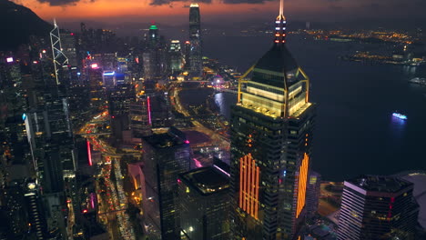 inclinación aérea hacia abajo del horizonte de hong kong y el puerto de victoria después de la puesta del sol - prominente plaza central de rascacielos en primer plano, distrito financiero central en segundo plano