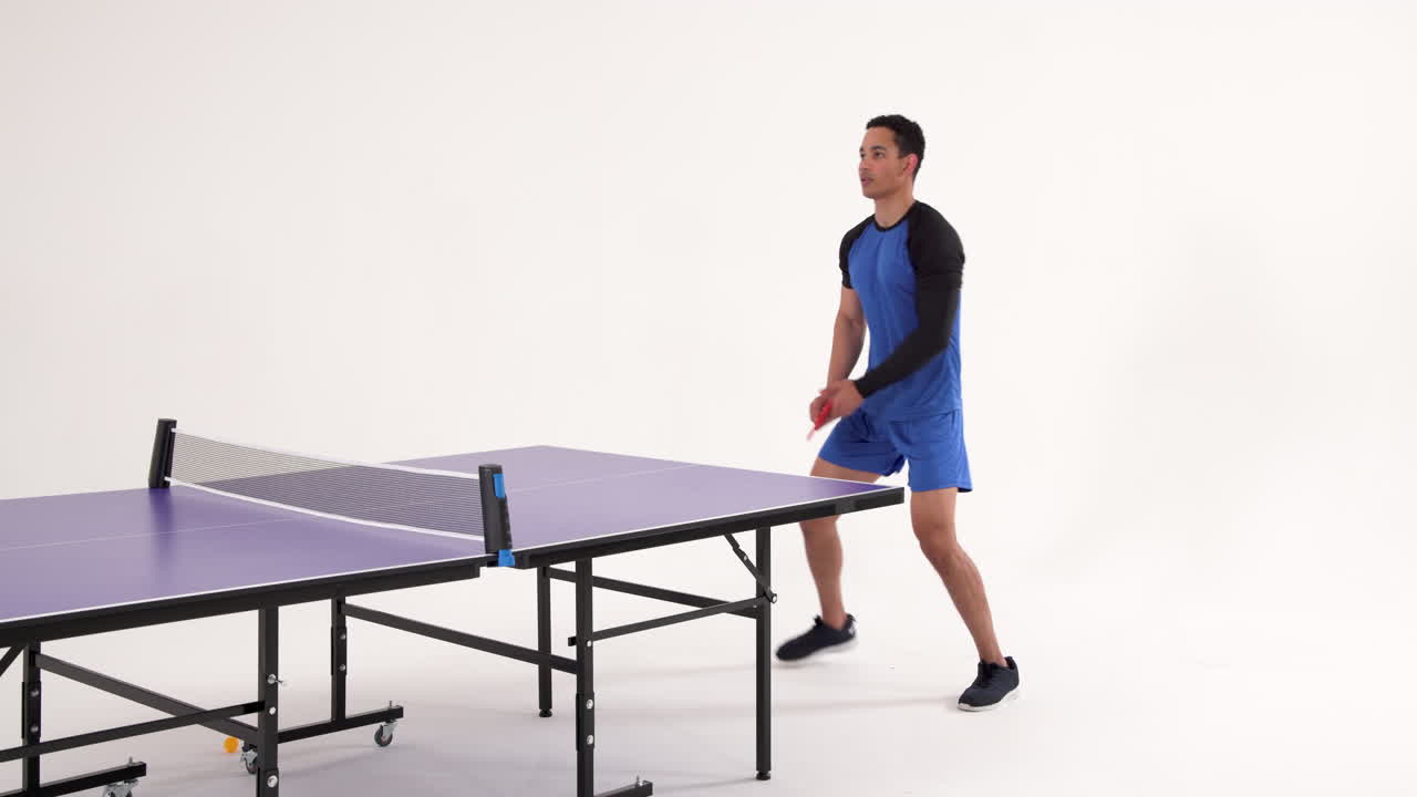 Playing table tennis, man hitting ball with paddle in studio setting