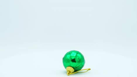 bola brillante verde navideña con mango dorado girando sobre un fondo blanco.