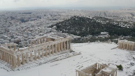 Aerial-drone-view-over-the-Parthenon,-overlooking-the-city-of-Athens,-exceptional-snowy-day-in-Greece