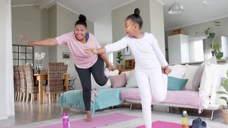 happy unaltered african american mother and daughter doing yoga stretching at home, in slow motion