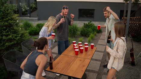 A-confident-brunette-girl-throws-a-small-white-ball-and-hits-a-cup-of-beer-during-a-drinking-game-at-a-company-party-in-the-courtyard-of-a-country-house