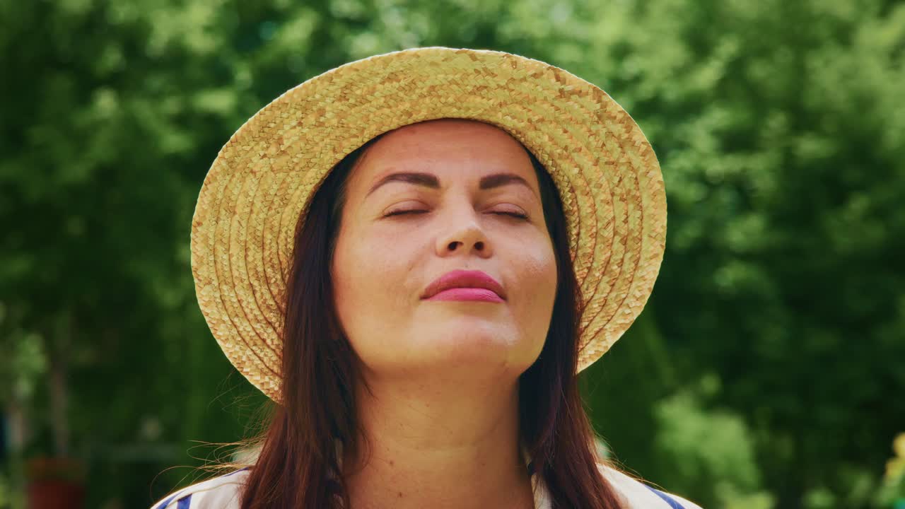 Donna che si gode la natura all'aperto, con un cappello di paglia, gli occhi chiusi e un'espressione serena