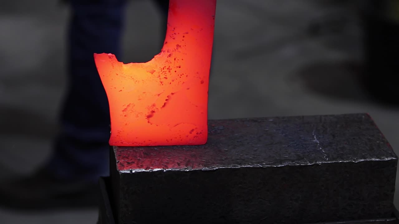 Blacksmiths forging hot metal with hammer in workshop