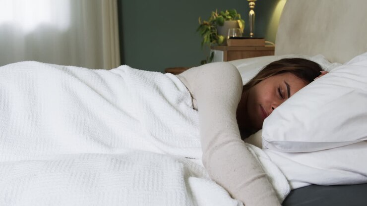 Kvinde sover fredeligt i et hyggeligt soveværelse, pakket ind i et hvidt tæppe, med plads til tekst