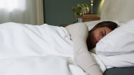 Woman peacefully sleeping in cozy bedroom, wrapped in white blanket, copy space