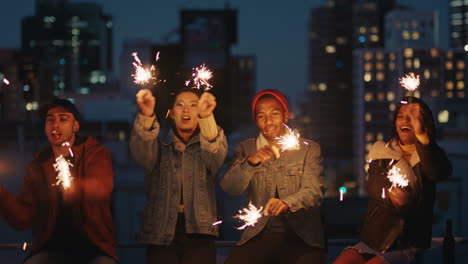 happy friends holding sparklers celebrating new years eve on rooftop at sunset having fun enjoying holiday party celebration