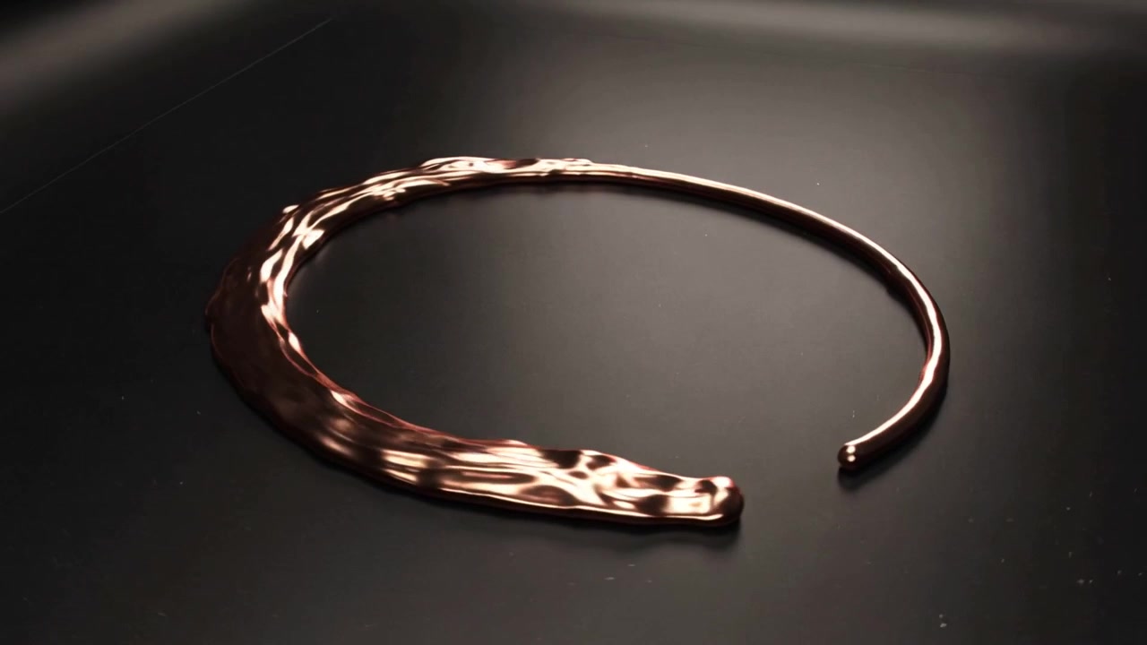 Una banda fusa che si forma in una fessura, un anello metallico aperto che cresce in senso orario su una superficie lucida, luce a raggiera.