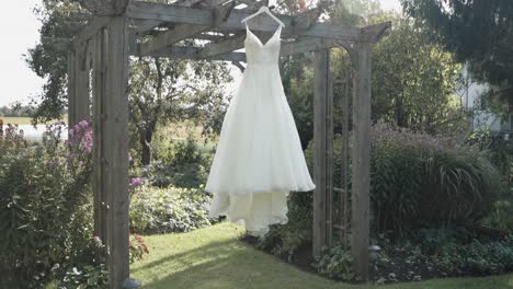 Beautiful-reveal-of-a-wedding-dress-hanging-from-a-patinaed-wooden-pergola-in-a-garden-at-the-Strathmere-Resort-in-Ottawa