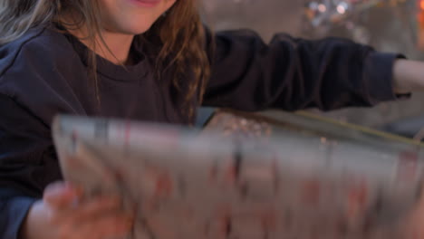 Close-Up-of-Surprised-and-Excited-young-girl-opening-Box-with-presents-in-front-of-Christmas-decoration-with-gifts-and-packages-on-santa-sledge