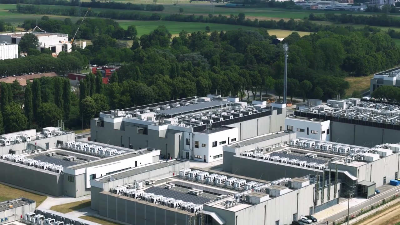 Aerial footage of a large-scale data center complex featuring multiple buildings with rooftop cooling systems and solar panels for sustainability