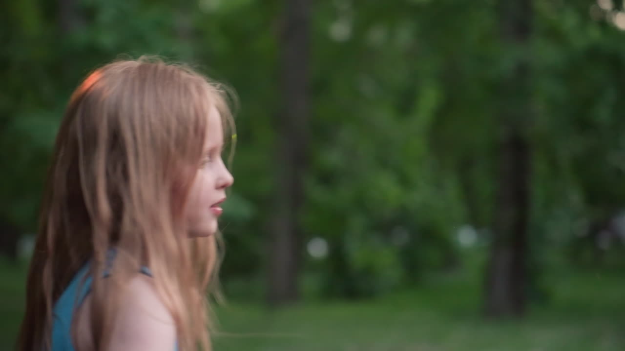 close up side view of school age girl pushing friend on wooden chain swing in blurred park playground capturing playful childhood interaction and summer fun among trees in gentle evening light
