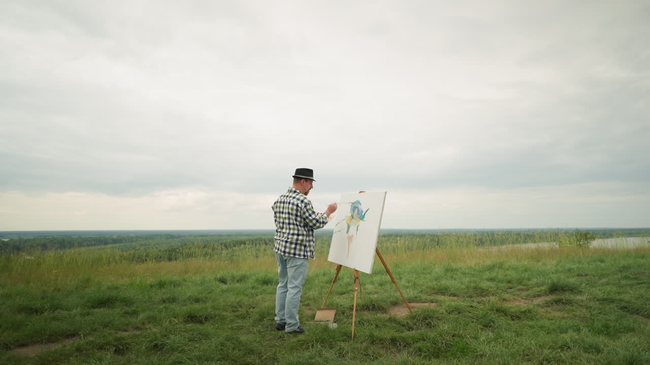 A painter wearing a hat, checkered shirt, and jeans is deeply focused on creating a masterpiece on a canvas, set in the middle of a lush grassy field beside a lake under a cloudy sky