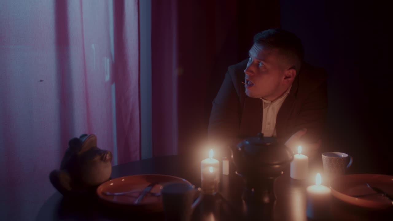 Man Sitting Alone at a Table with Candles in a Dark Room