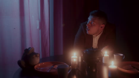 man sitting alone at a table with candles in a dark room