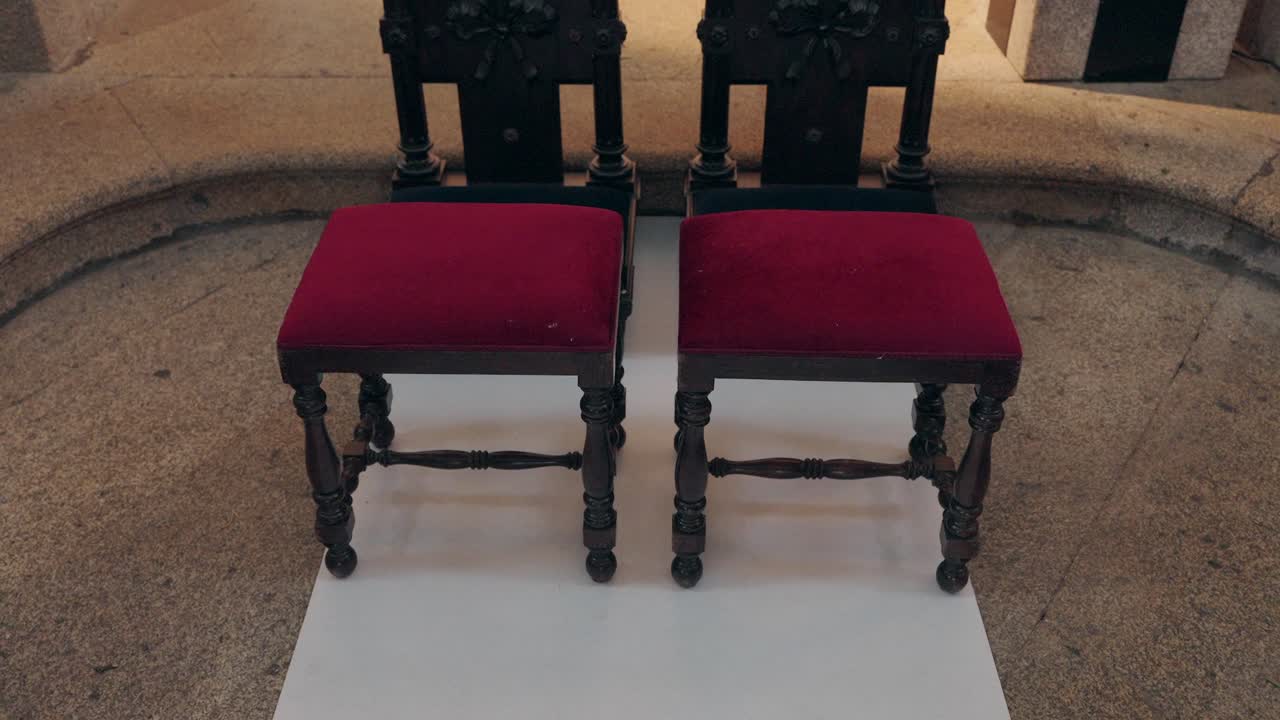 two antique wooden chairs with red cushions set at church altar for wedding ceremony