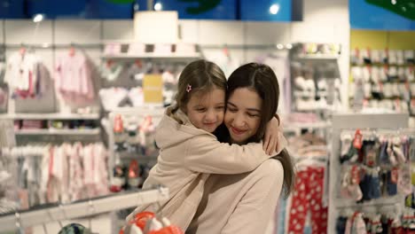madre encantadora buscando ropa en la percha con su hija en el centro comercial