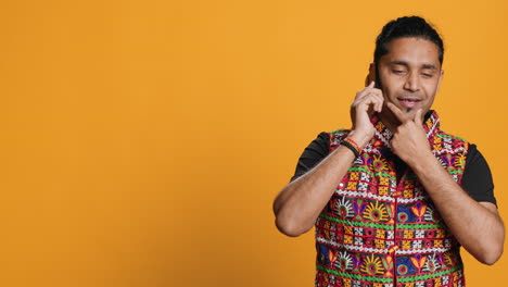 happy man in traditional clothing talks with friend on call, studio background