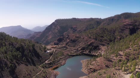 drone aéreo volando hacia adelante sobre la línea de árboles alrededor de un embalse de lago en las montañas de gran canaria, españa