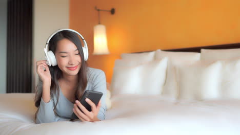 a lively asian girl wearing on-ear headphones is listening to music and dancing while holding her cellphone in hand, excited