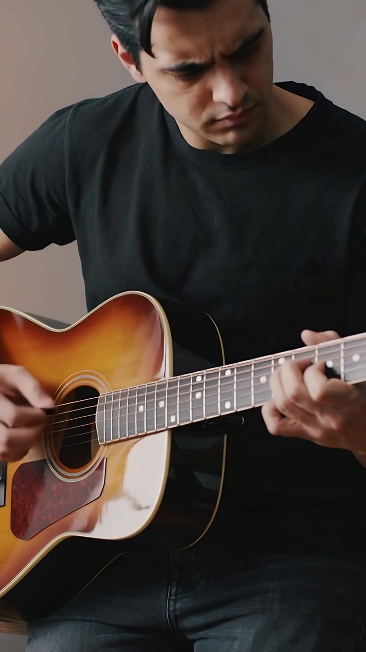 Video verticale: Uomo che suona e si esercita con gli accordi, mentre la mano destra si muove su una chitarra acustica a casa, indossando una maglietta nera.