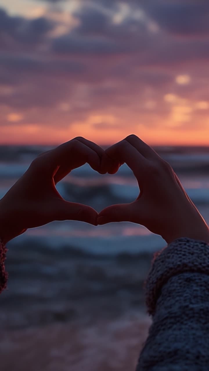 Un tramonto affascinante risplende mentre le mani formano un cuore, a simboleggiare amore e connessione tra le serene onde dell'oceano.