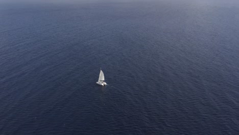 elevated aerial arc around single catamaran sailing in wide open ocean