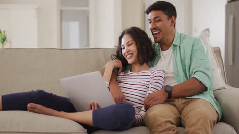 Hispanic-couple-sitting-on-sofa-looking-at-laptop-discussing