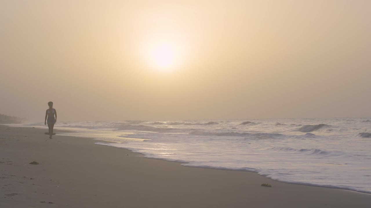 Young woman walks towards camera on the seashore during sunset