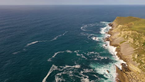 vuelo en el mar cantábrico con un dron donde vemos un acantilado en forma de península, haciendo girar una cámara, descubrimos el cielo con el mar en el horizonte y vemos algunas islas en españa