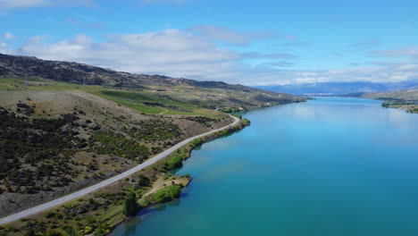 drone em torno da estrada que corre ao longo do lago azul da nova zelândia