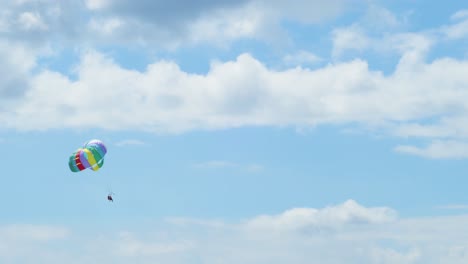 view of couple flying in a parachute pulled by a boat over a blue sky with white clouds