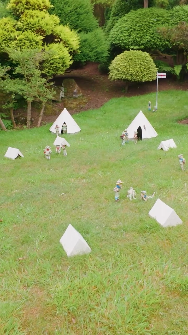Campeggio modello al Godshill Model Village visto in un'orbita lenta, che mostra tende in miniatura, camper e un piccolo veicolo tra prati curati e arbusti da giardino. Formato verticale per i social media