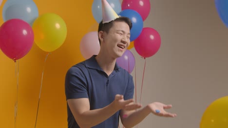 Studio-Portrait-Of-Man-Wearing-Party-Hat-Celebrating-Birthday-Blowing-Paper-Confetti