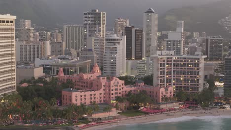 Backwards-aerial-view-of-luxury-resorts-in-Waikiki-after-sunset-in-Honolulu