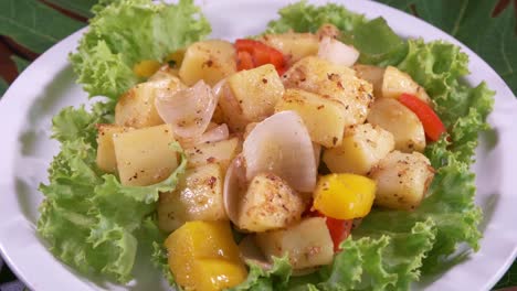 Frischer-Kartoffelsalat-Mit-Zwiebeln-Und-Paprika,-Dekoriert-Mit-Frisch-Geschnittenem-Salat-Auf-Einem-Weißen-Teller,-Der-Sich-Mit-Nahaufnahme-Dreht