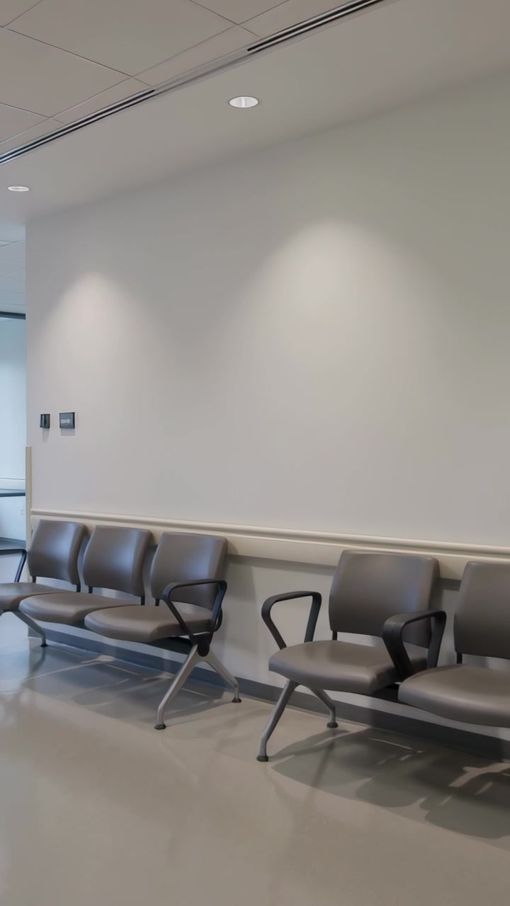 Video verticale: Telecamera che si muove lentamente mostrando sedili grigi in una sala d'attesa di una clinica, rivelando pannelli di controllo.