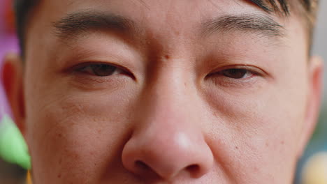 close-up macro portrait of asian man face smiling, brown gauy eyes looking at camera blink wink