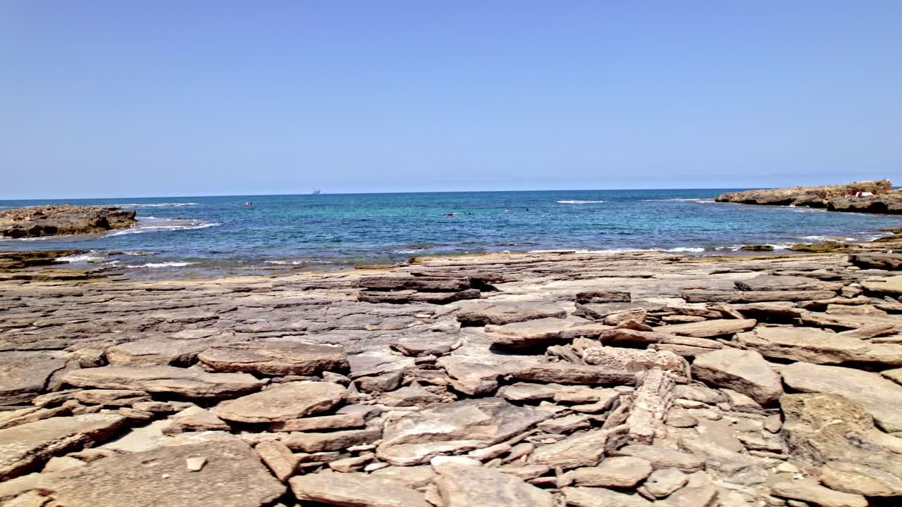 Drone captures a wide view of a rocky sandstone coastline with turquoise sea under a clear blue sky on a sunny day.