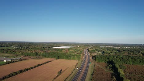 Aerial-drone-shot-over-car-movement-along-two-way-highway-along-rural-countryside-with-autumn-blue-skies-on-a-sunny-day